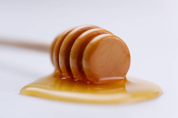 Wooden spoon with a drop of delicious liquid honey on a white background. Close-up. Isolated. - Zdjęcie, obraz