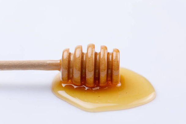Wooden spoon stick with a drop of fragrant honey on a white background. Close-up. Isolated. - Foto, afbeelding