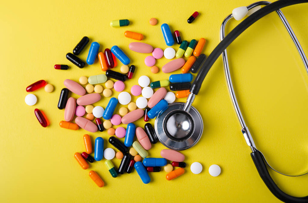 Pills capsules stethoscope medicine health on yellow background top view - 写真・画像