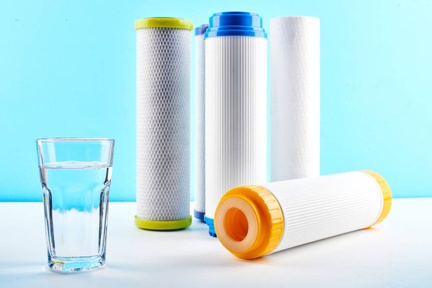 Water filters. Carbon cartridges and a glass on a white blue background. Household filtration system. - Фото, зображення