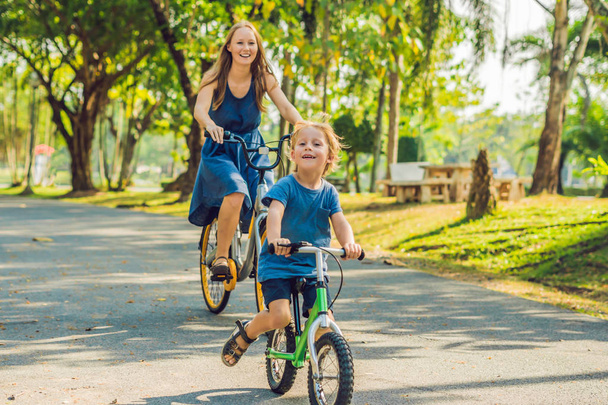 Happy family is riding bikes outdoors and smiling. Mom on a bike and son on a balancebike - Photo, Image