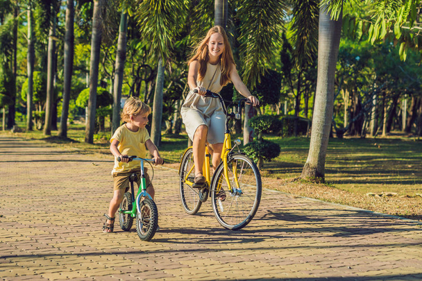 Une famille heureuse fait du vélo à l'extérieur et sourit. Maman sur un vélo et fils sur un balancebike
 - Photo, image