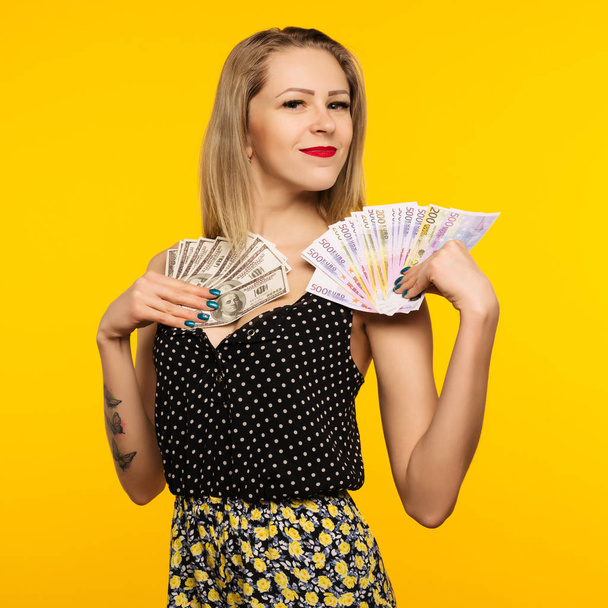 Φωτογραφία: ευτυχισμένη γυναίκα στέκεται απομονωμένο, πάνω από το κίτρινο φόντο. Βλέπουν φωτογραφική μηχανή κρατά χρήματα - εικόνα - Φωτογραφία, εικόνα