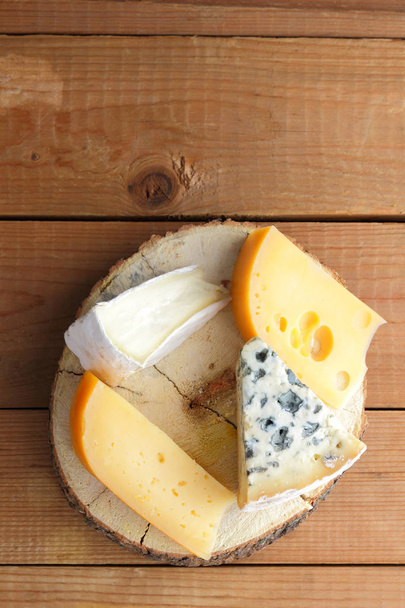 Assortment of cheeses on wooden boards. Camembert, hard yellow cheese, dorblu on wooden stand. Top view - Foto, Bild