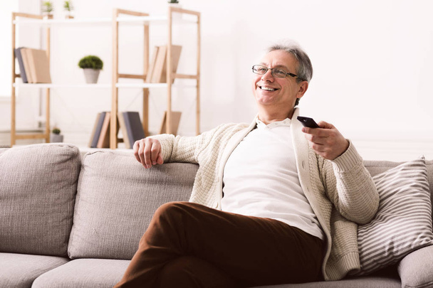 Happy senior man watching tv, sitting on couch - Fotó, kép