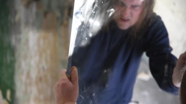 depressiver und wütender Mann hält einen Spiegel und blickt ihn wütend an - Filmmaterial, Video
