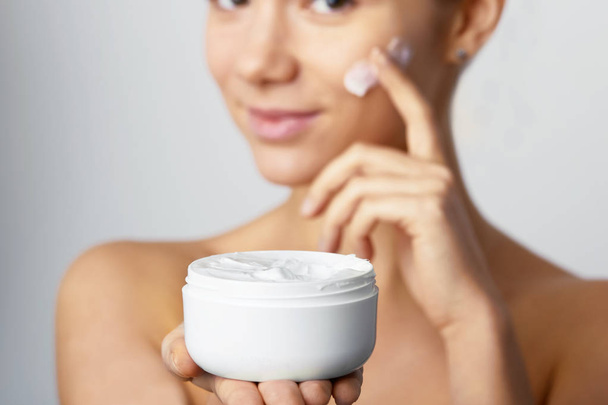 Hands of a woman about to apply face cream. Holding Moisturizing Lotion.Close-up young beautiful face of girl applying moisturize cream - Фото, изображение