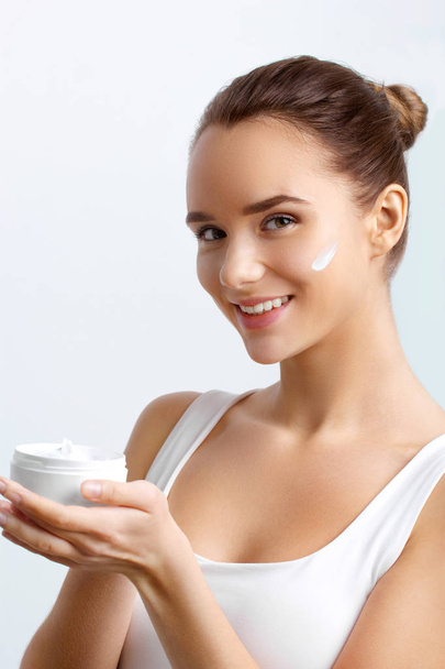 Beauty Concept. Taking good care of her skin. Attractive young woman looking at camera and smiling.Portrait of attractive female with healthy smooth facial clean skin holding bottle. Face Skin Care. - Photo, Image