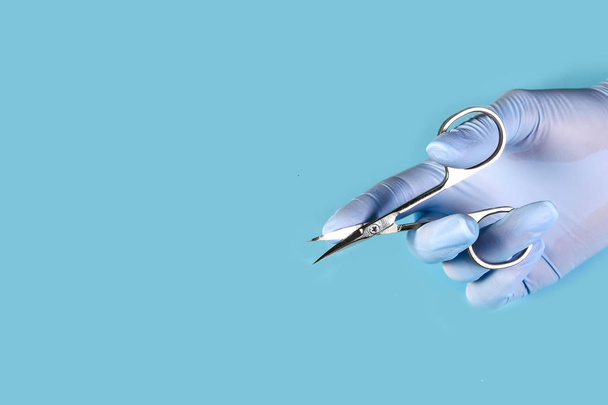 master paznokcie w niebieskich rękawiczkach posiada nożyczki narzędzie manicure. zestaw akcesoriów do manicure na niebieskim tle widok z góry. Skład karty z miejscem na tekst. - Zdjęcie, obraz