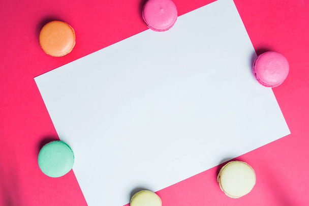 Flat lay of white A4 paper on a bright pink background with colorful macaroons. Copy space for text and advertising - Foto, Bild