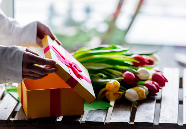 verpakken van prachtige tulpen in de buurt van de doos van de gift op houten tafel - Foto, afbeelding