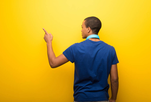 Afro-amerikai ember mutatva vissza a mutatóujjával sárga alapon kék pólóban - Fotó, kép