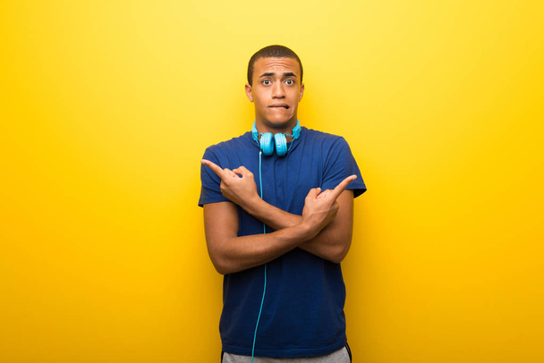 African american man met blauw t-shirt op gele achtergrond wijzen op de twijfels laterals - Foto, afbeelding