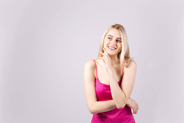 Studio shot of gorgeous young blonde woman with long straight hair wearing sexy lillac slim fit cocktail dress and smiling. Gray isolated background, copy space, close up, portrait. - Foto, imagen
