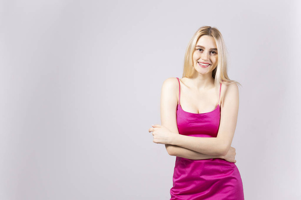 Studio shot of gorgeous young blonde woman with long straight hair wearing sexy lillac slim fit cocktail dress and smiling. Gray isolated background, copy space, close up, portrait. - Fotó, kép
