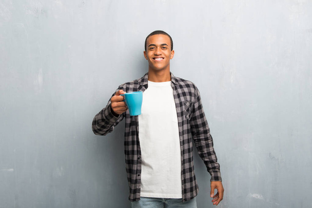 Νεαρός αφρικανική αμερικανική άνθρωπος με καρώ πουκάμισο κρατώντας ένα ζεστό καφέ - Φωτογραφία, εικόνα