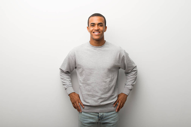 Hombre afroamericano sobre fondo blanco posando con los brazos en la cadera y riendo mirando hacia el frente
 - Foto, imagen