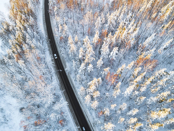 Aerial view of a car on winter road in the forest. Winter landscape countryside. Aerial photography of snowy forest with a car on the road. Captured from above with a drone. Aerial photo. Car in motion - Zdjęcie, obraz