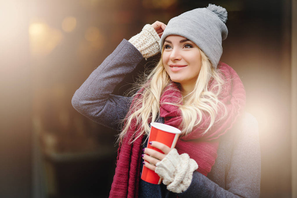 Close-up portrait of young blonde woman drinking coffe and enjoying the morning on the street. - Image - Foto, Bild