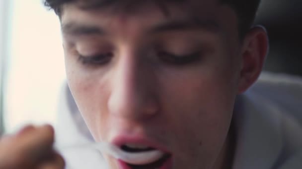 Close-up of the face of a guy eating yogurt with a spoon. - Felvétel, videó