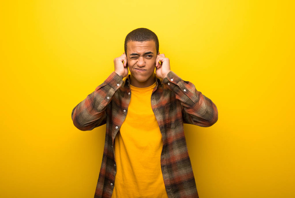 Młody człowiek african american na żywe żółtym tle obejmujące uszy rękami. Sfrustrowany wyrażenie - Zdjęcie, obraz