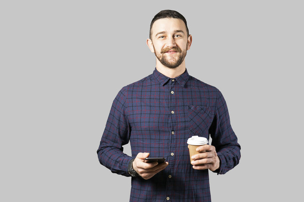 Young handsome man with facial hair holding posing over gray wall with a lot of copy space for text. Portrait of confident bearded male, wearing hipster slim fit checkered shirt. Isolated, background. - Фото, изображение