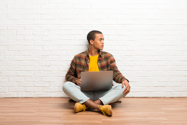 Αφρικανική αμερικανική άνθρωπος που κάθεται στο πάτωμα με το laptop του σε πλάγια θέση - Φωτογραφία, εικόνα