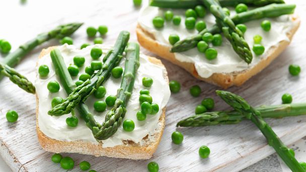 Appetizer bruschetta, toast with Asparagus, Peas and creamy soft cheese on white board. healthy food. - Photo, Image