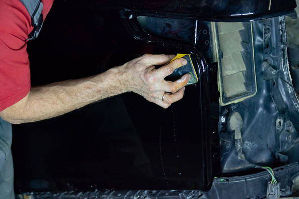 Le polisseur couvre la carrosserie du véhicule avec de la cire spéciale pour protéger la voiture contre les rayures et les dommages mineurs, frottant la surface du VUS noir avec une éponge
. - Photo, image