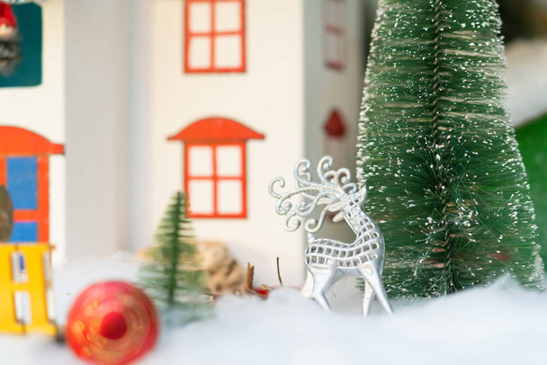 Shiny silver filigree reindeer ornament in a Christmas scene with snowy trees and a quaint colorful model house - Foto, Bild