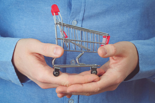 Shopping concept. A man in a blue shirt holds a cart in his hands. - Φωτογραφία, εικόνα