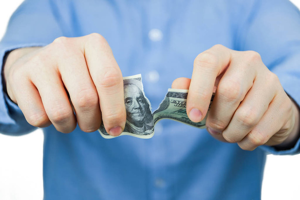 Έννοια του παραίτηση από δολάρια ΗΠΑ. Ένας άνδρας με ένα μπλε πουκάμισο κατέχει εκατό δολάρια ΗΠΑ και τα δάκρυα επάνω. - Φωτογραφία, εικόνα