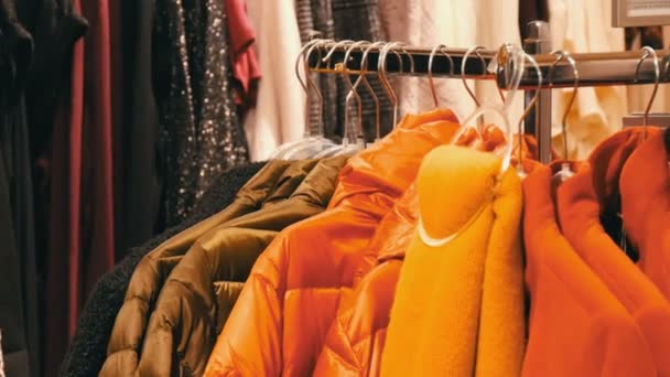 Κομψό ζεστά ρούχα που κρέμονται στη γραμμή στις κρεμάστρες σε ένα κατάστημα ιματισμού σε ένα εμπορικό κέντρο. - Πλάνα, βίντεο