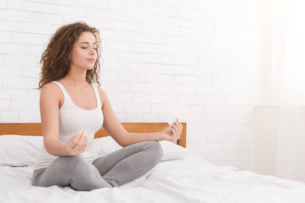 Молодая женщина медитирует в позе лотоса на кровати
 - Фото, изображение