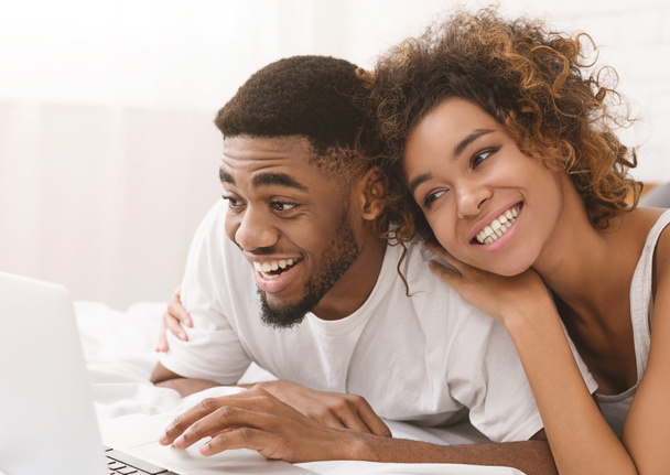 Genç siyah çift yatakta yatarken ve dizüstü bilgisayar kullanarak. - Fotoğraf, Görsel