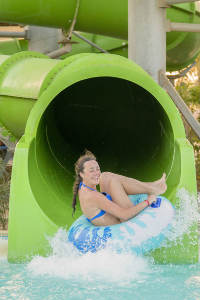 ウォーター スライド ダウンしている女性。幸せな女は、アクア公園でオレンジ色のスライドでゴム輪の下に行きます。夏休み。週末リゾート。垂直写真. - 写真・画像