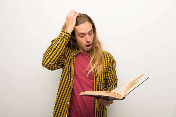 Blond man with long hair and with checkered shirt surprised while enjoying reading a book - Valokuva, kuva