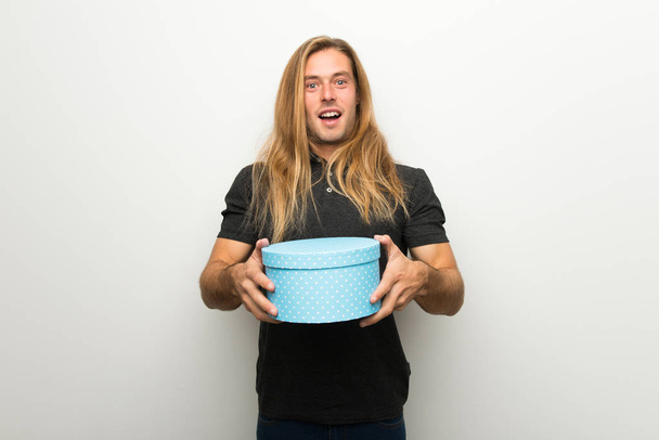 Blond man with long hair over white wall surprised because has been given a gift - Photo, Image