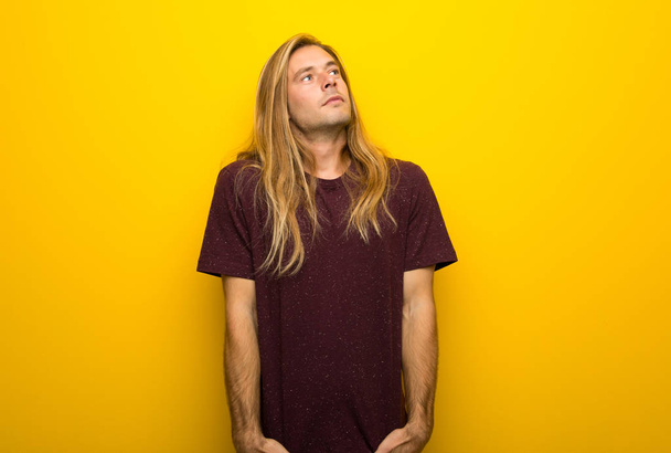 Homme blond aux cheveux longs sur un mur jaune levant les yeux avec un visage sérieux
 - Photo, image