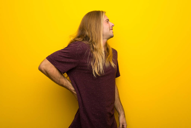 Blond man with long hair over yellow wall suffering from backache for having made an effort - Photo, Image
