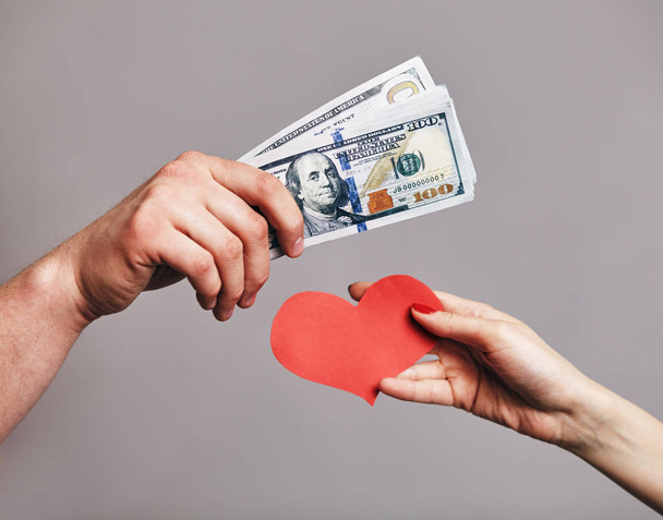 a Male hand holding a pack of money trying to buy a red hearts from female hand - Buying love concept - Φωτογραφία, εικόνα