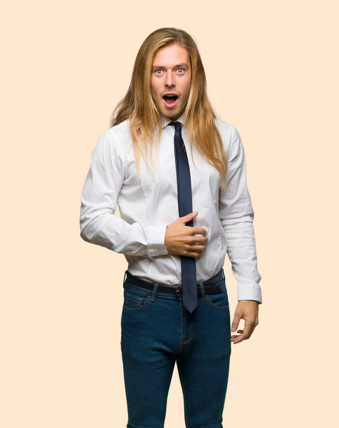 Uomo d'affari biondo con i capelli lunghi con sorpresa e espressione facciale scioccata su sfondo isolato
 - Foto, immagini