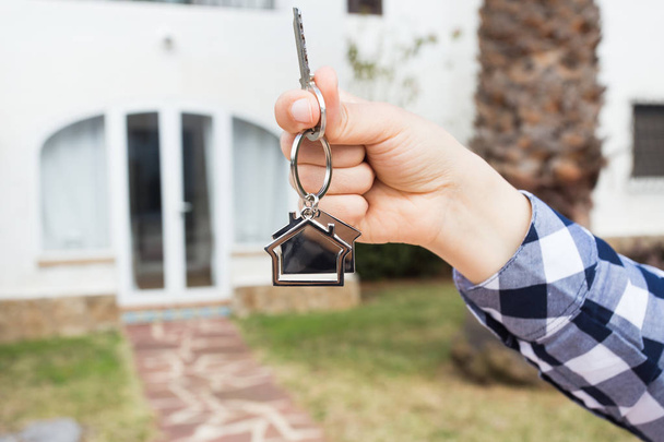 Концепция недвижимости и собственности - Мбаппе держит ключи от дома на брелоке в форме дома перед новым домом
. - Фото, изображение