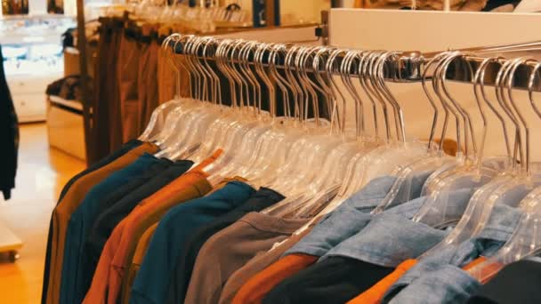 Ropa juvenil de moda colgada de perchas en una tienda de ropa en un centro comercial
. - Metraje, vídeo