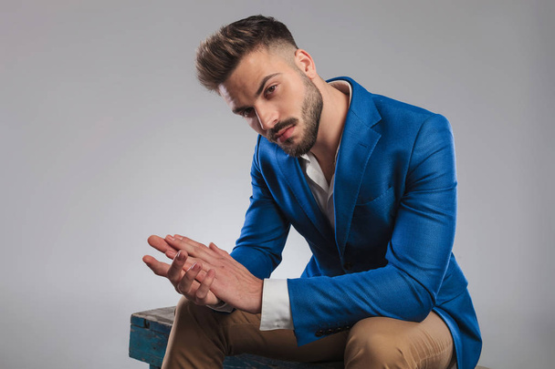 sexy smart casual man sitting on wooden bench and holding palms together - Photo, Image