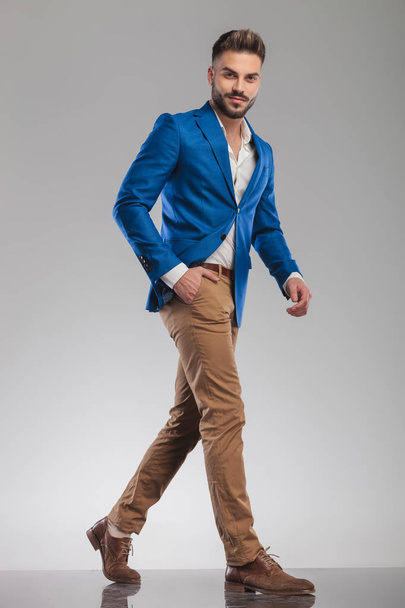 relaxed smart casual man in blue suit walking to side on light grey background, full length picture - Foto, Imagen