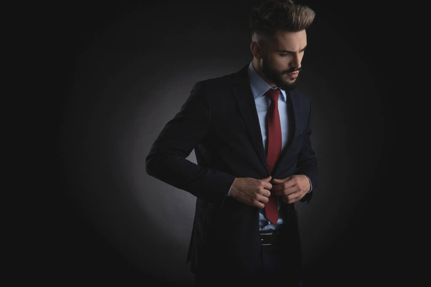 Lacivert takım elbise kadar düğmelerini ve yan duran siyah arka plan üzerine isteyen çekici işadamı portresi - Fotoğraf, Görsel