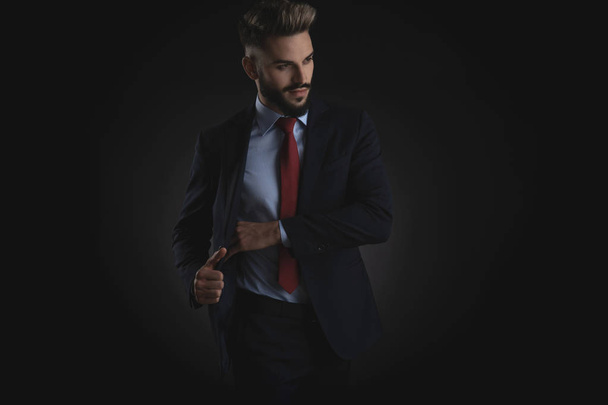 attraktiver Geschäftsmann pickt etwas aus der Innentasche eines Navy-Anzugs und blickt auf schwarzem Hintergrund zur Seite, Porträtbild - Foto, Bild