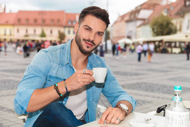 glimlachend casual man zit in de stad aan een tafel en drinken koffie, portret beeld - Foto, afbeelding