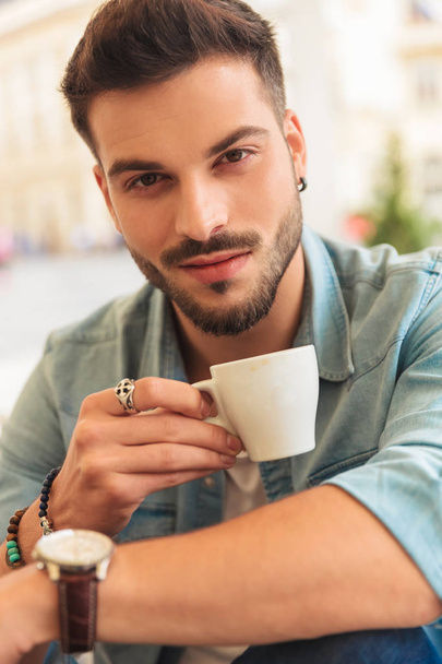 portrait of smiling casual man having a coffee break at table in the city center while holding cup - Foto, imagen